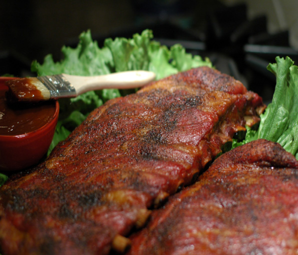 A plate of ribs with sauce and lettuce.