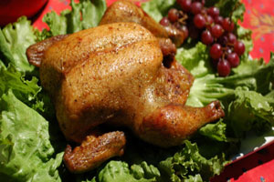 A chicken sitting on top of some lettuce and grapes.